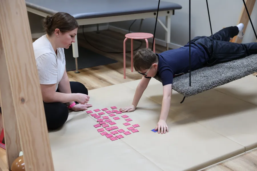 An occupational therapist working with a child lying on a swing over a floor activity during a session